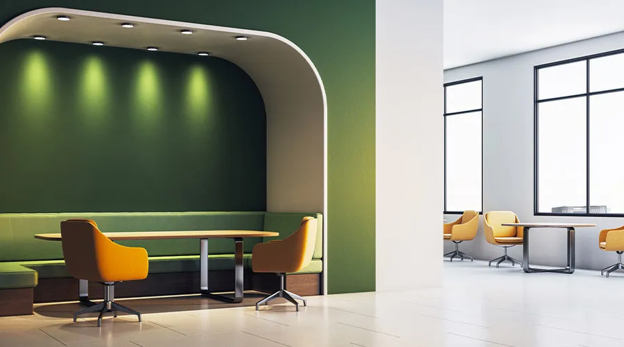 Spazio lounge in ufficio con parete verde, sedute imbottite e tavolo per riunioni informali in ambiente luminoso e moderno