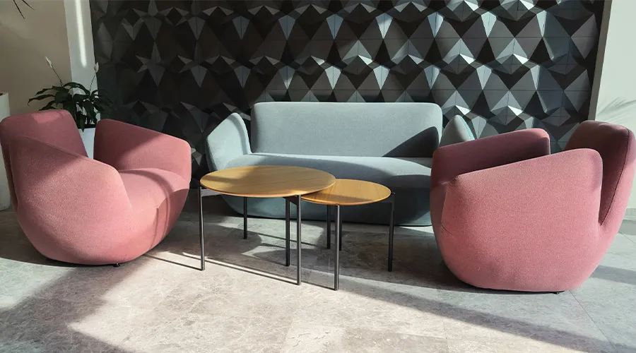 Zona relax in ufficio con poltrone imbottite colorate, tavolini bassi e parete 3d geometrica in ambiente moderno