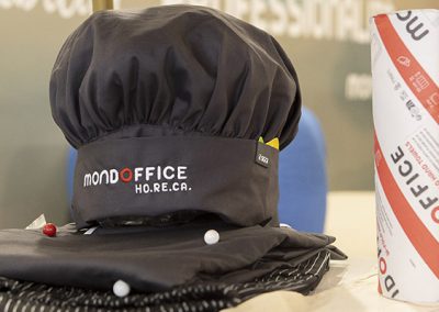 Cappello da chef e grembiule con logo Mondoffice Ho.Re.Ca. esposti alla fiera Hospitality di Riva del Garda
