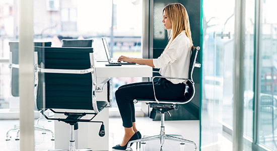 Donna seduta correttamente su una sedia ergonomica davanti al computer
